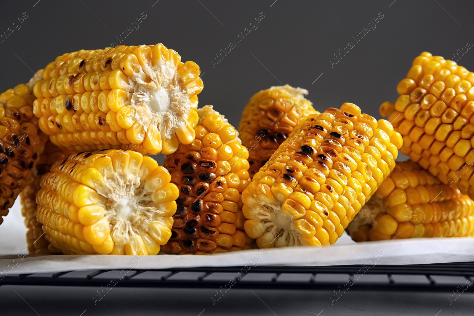 Photo of Cooling rack with grilled corn cobs on table against gray background, closeup