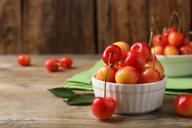 Photo of Sweet red cherries in bowl on wooden table, space for text