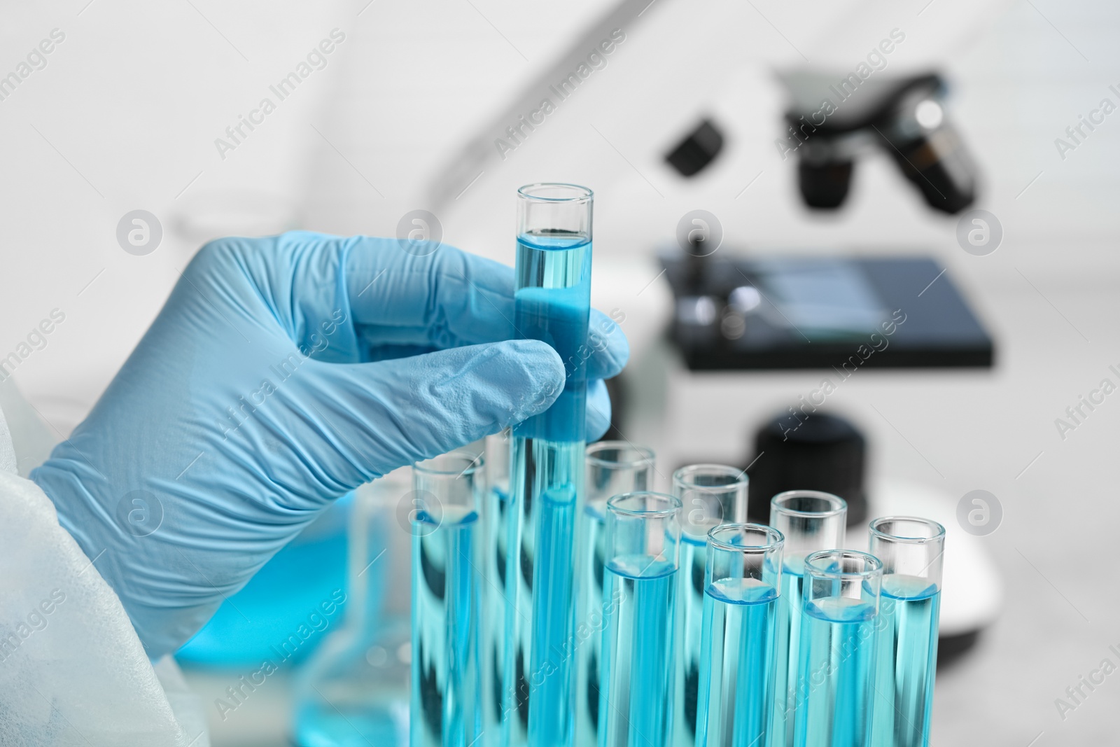 Photo of Scientist taking test tube with light blue liquid in laboratory, closeup