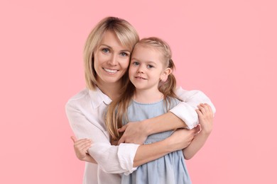 Photo of Mother hugging her happy daughter on pink background