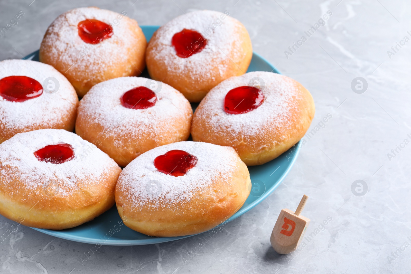 Photo of Hanukkah doughnuts with jelly and dreidel on grey table
