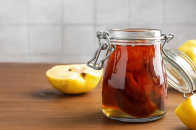 Photo of Tasty homemade quince jam in jar and fruits on wooden table, closeup. Space for text