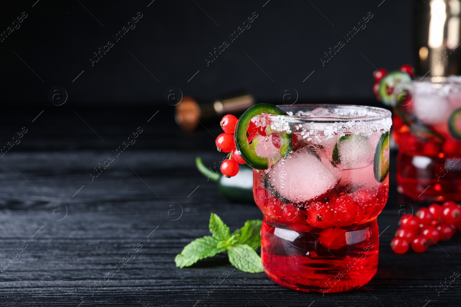 Photo of Spicy red currant cocktail with jalapeno on black wooden table. Space for text