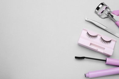 Flat lay composition with fake eyelashes, mascara brush and tools on light grey background. Space for text