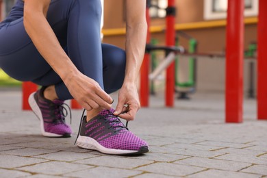 Woman tying shoelaces before training at outdoor gym, closeup. Space for text