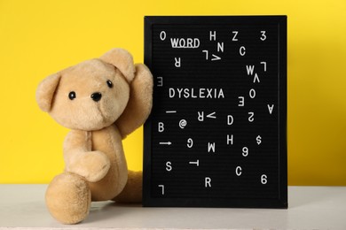 Photo of Black letter board with word Dyslexia and teddy bear on light table against yellow background