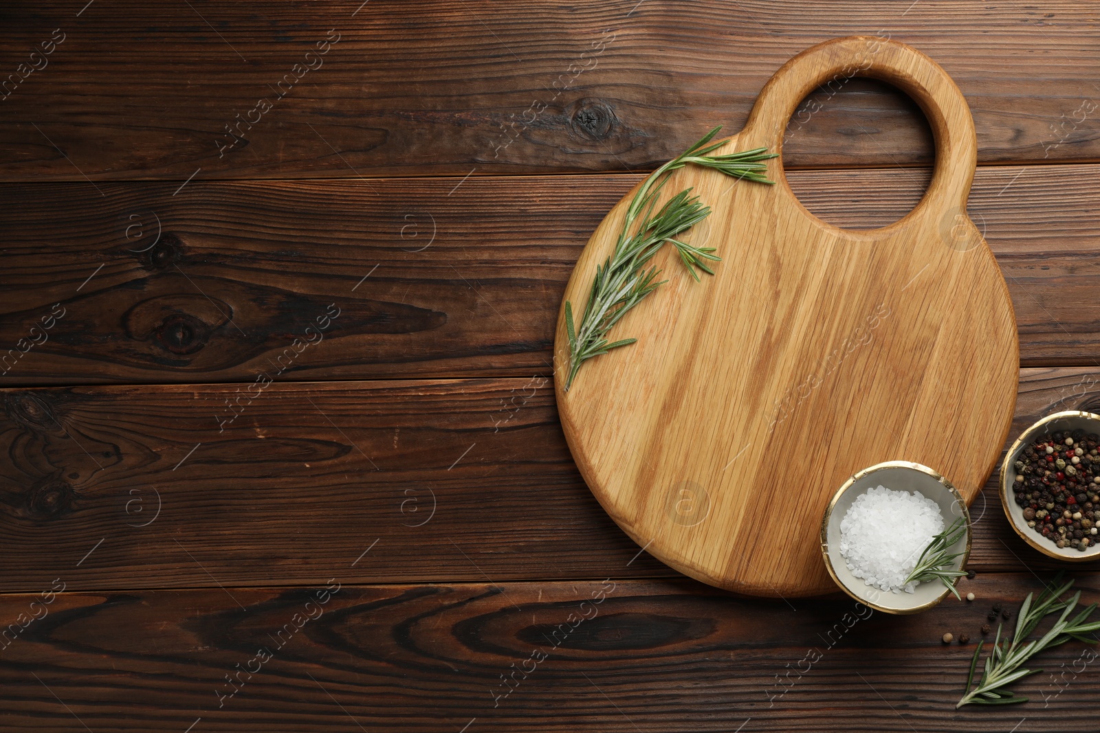 Photo of Cutting board, salt, pepper and rosemary on wooden table, flat lay. Space for text