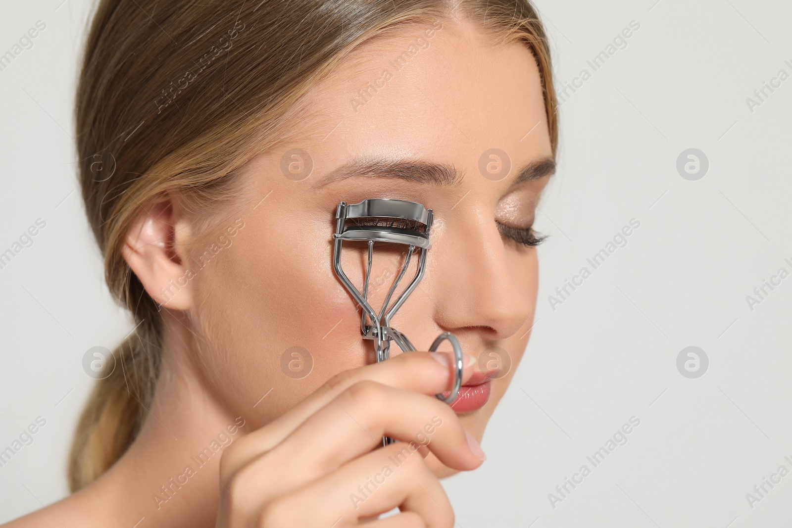 Photo of Young woman using eyelash curler on white background