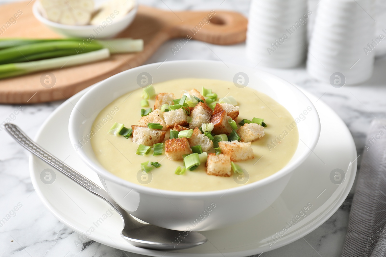 Photo of Tasty potato soup with croutons in bowl and spoon on white marble table