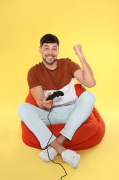 Emotional man playing video games with controller on color background