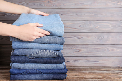 Woman folding stylish jeans on wooden table, closeup. Space for text