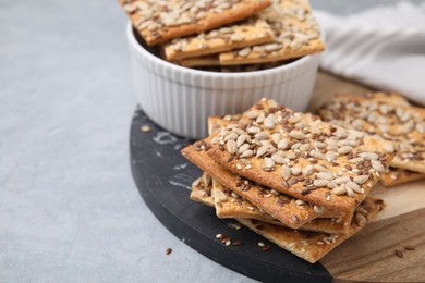 Photo of Cereal crackers with flax, sunflower and sesame seeds on grey table, closeup. Space for text