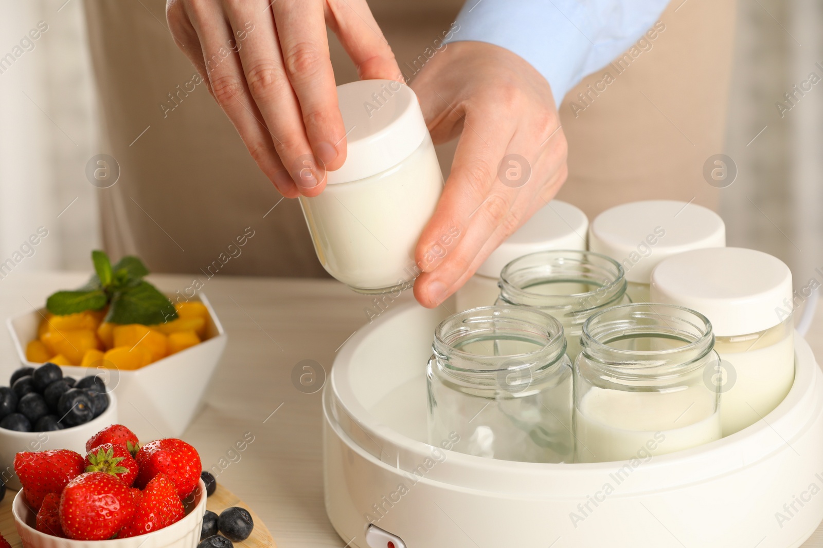 Photo of Woman making tasty yogurt at white wooden table indoors, closeup