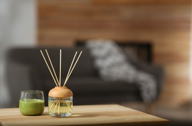 Photo of Aromatic reed air freshener and scented candle on table indoors. Space for text