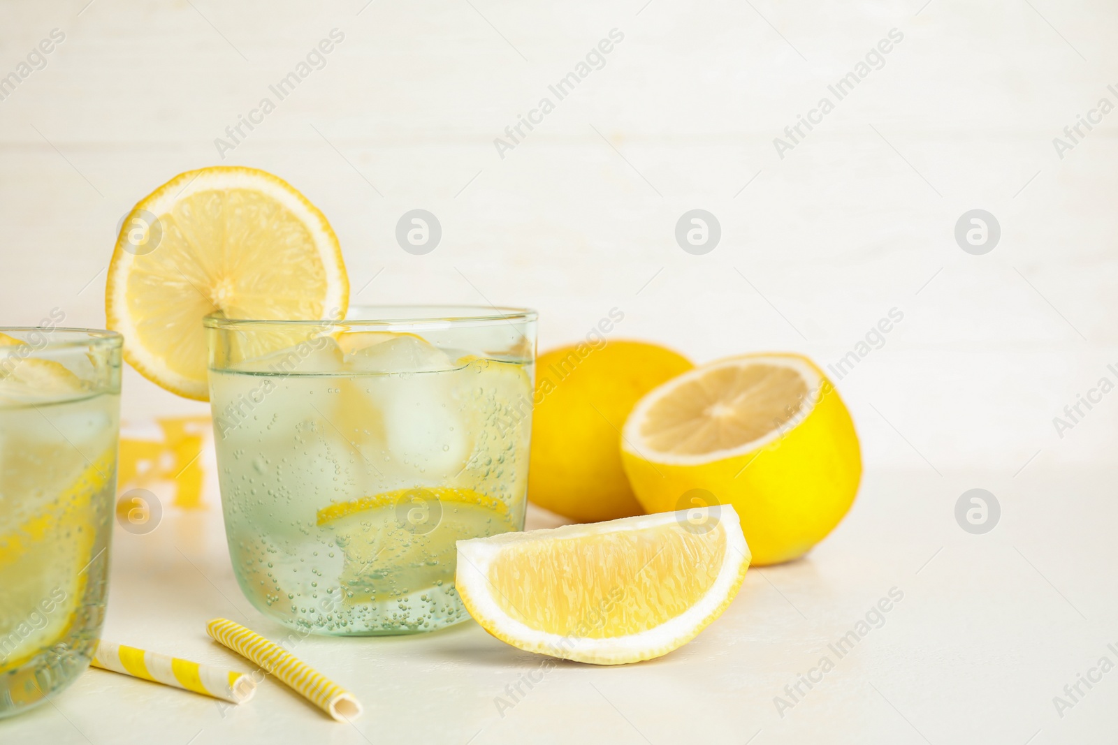 Photo of Soda water with lemon slices and ice cubes on white table. Space for text