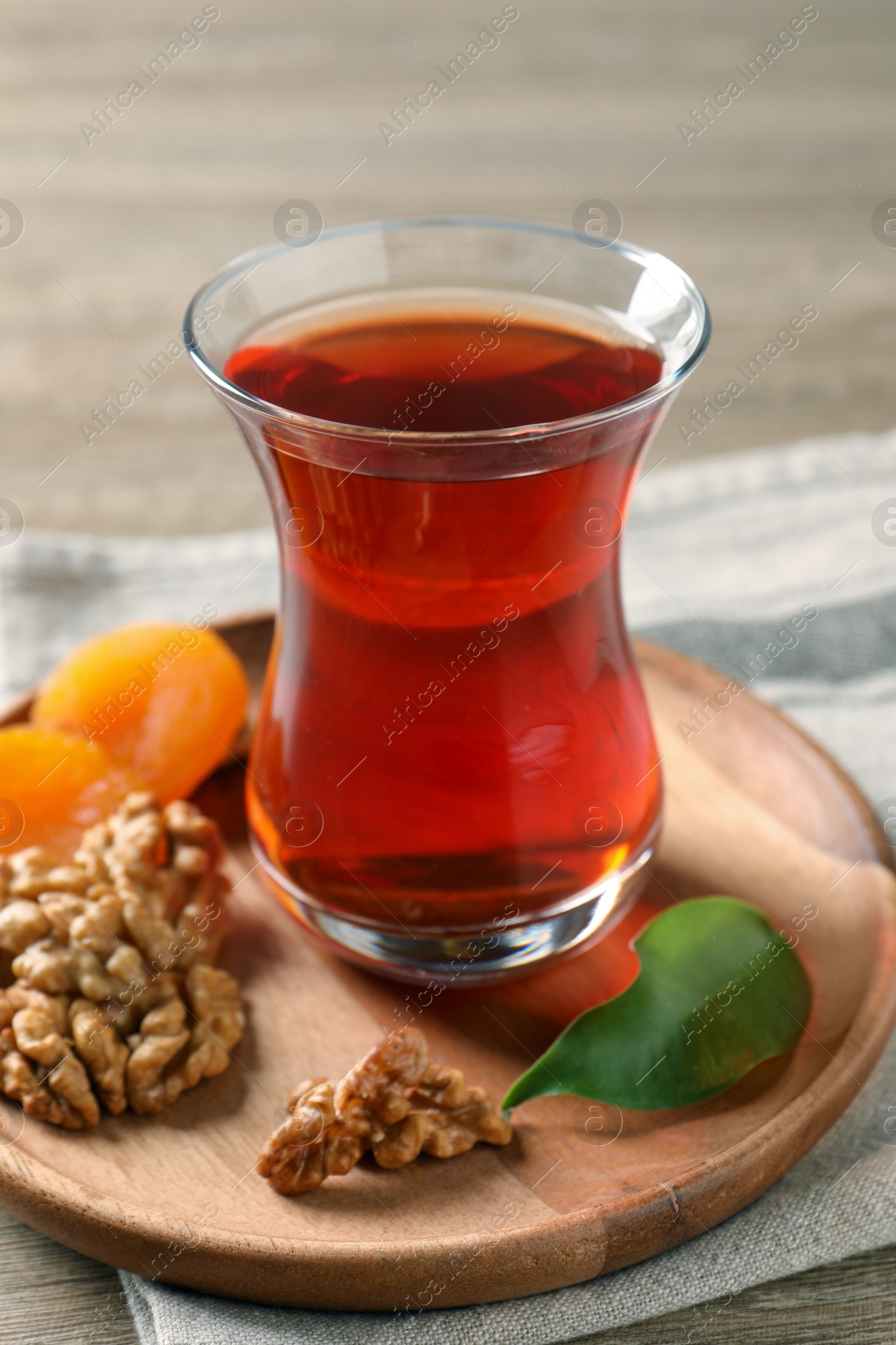 Photo of Board with glass of traditional Turkish tea, walnuts and dried apricots on wooden table, closeup