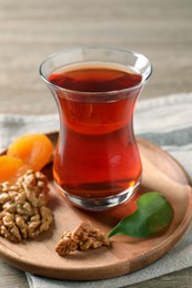 Photo of Board with glass of traditional Turkish tea, walnuts and dried apricots on wooden table, closeup