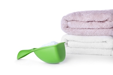 Laundry detergent in plastic measuring scoop and towels on white background