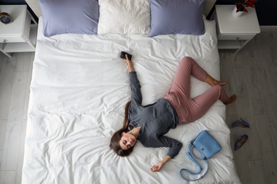 Photo of Exhausted woman with cup of coffee and purse sleeping fully dressed on bed at home, above view