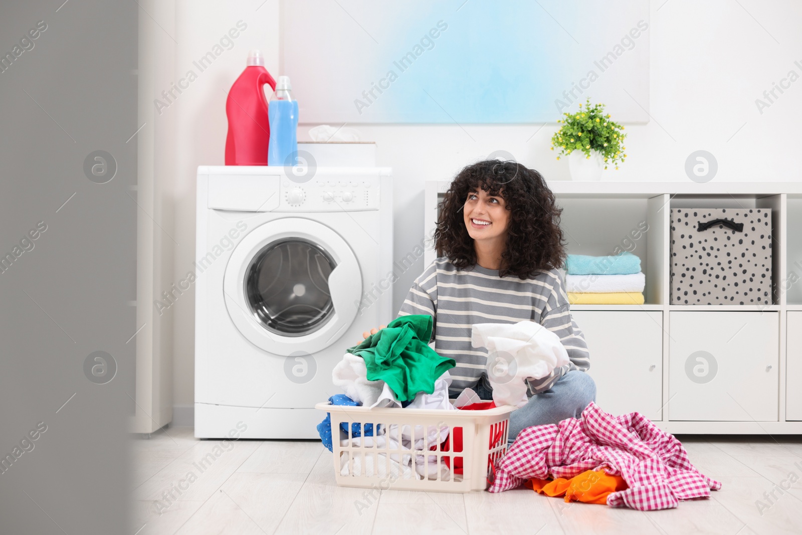 Photo of Happy woman with laundry near washing machine indoors