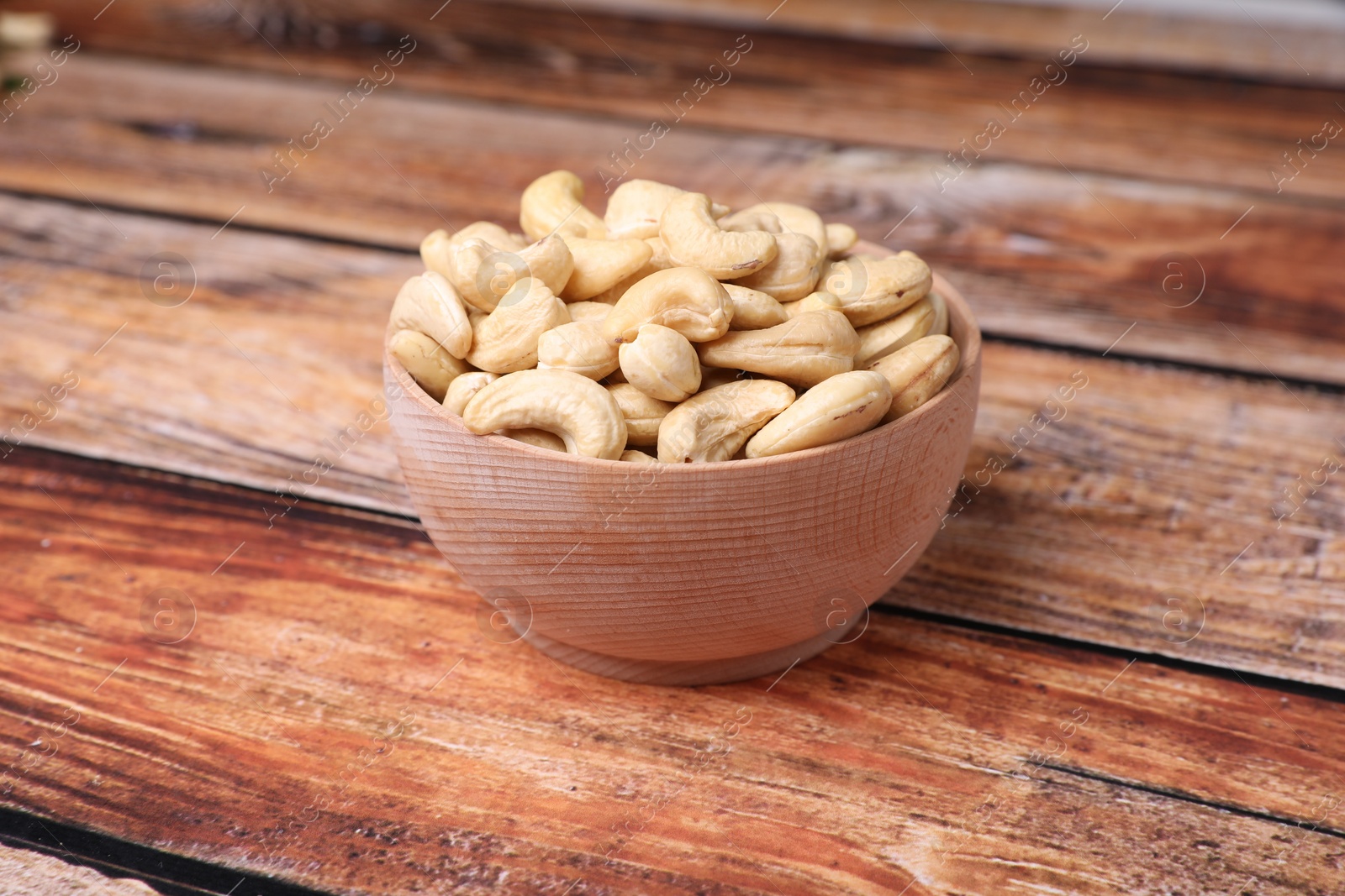 Photo of Tasty cashew nuts in bowl on wooden table