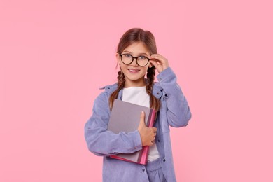 Smiling schoolgirl with books on pink background