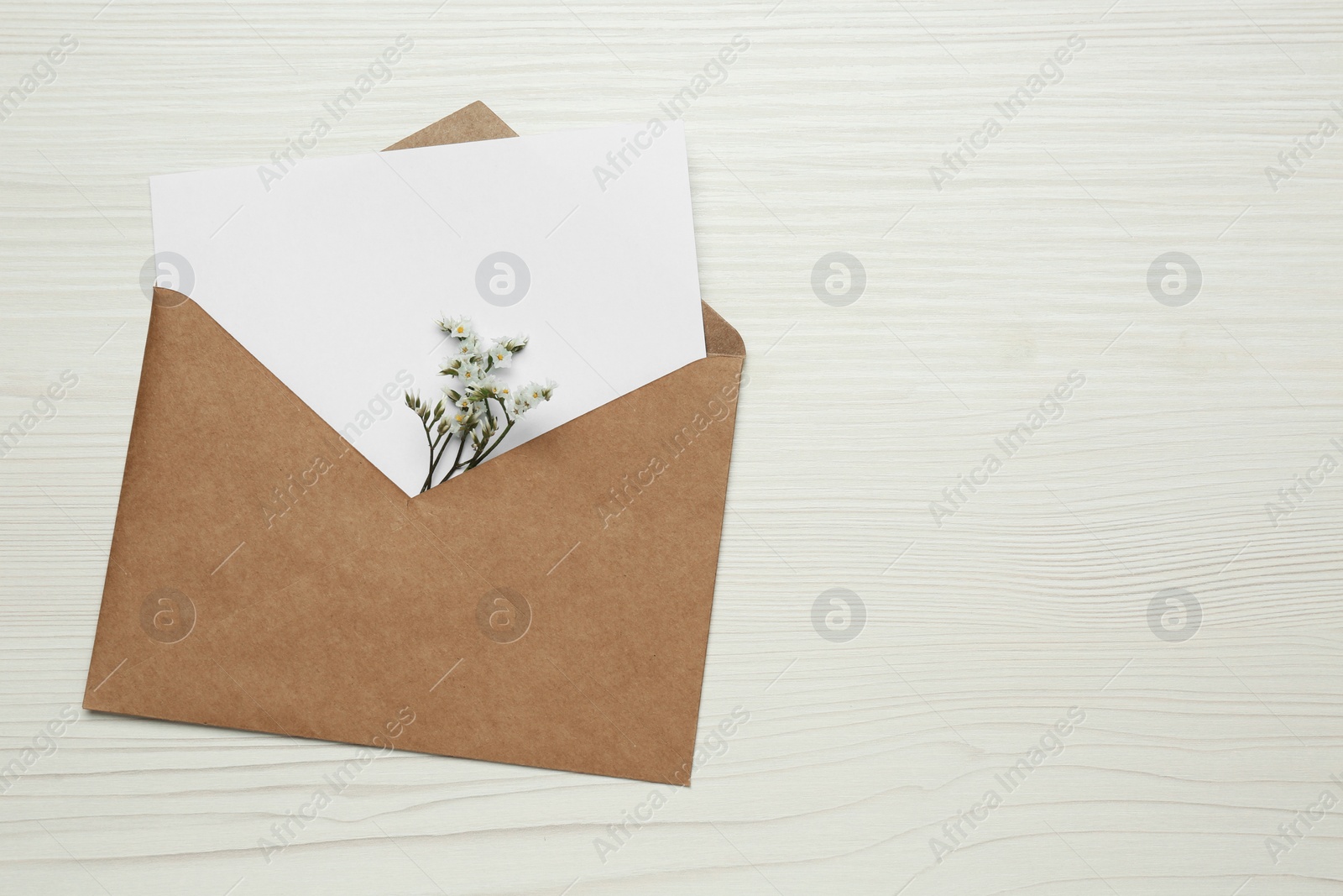 Photo of Envelope with blank paper card and flowers on white wooden table, top view. Space for text