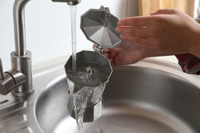 Photo of Woman washing moka pot (coffee maker) above sink in kitchen, closeup