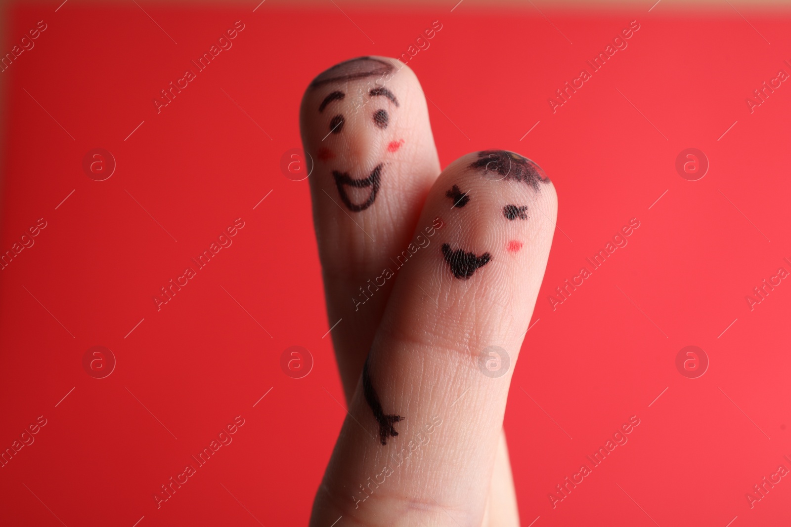 Photo of Two fingers with drawings of happy faces on red background. Spending time together