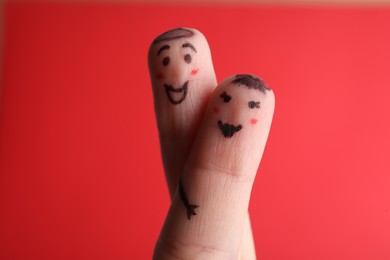 Photo of Two fingers with drawings of happy faces on red background. Spending time together