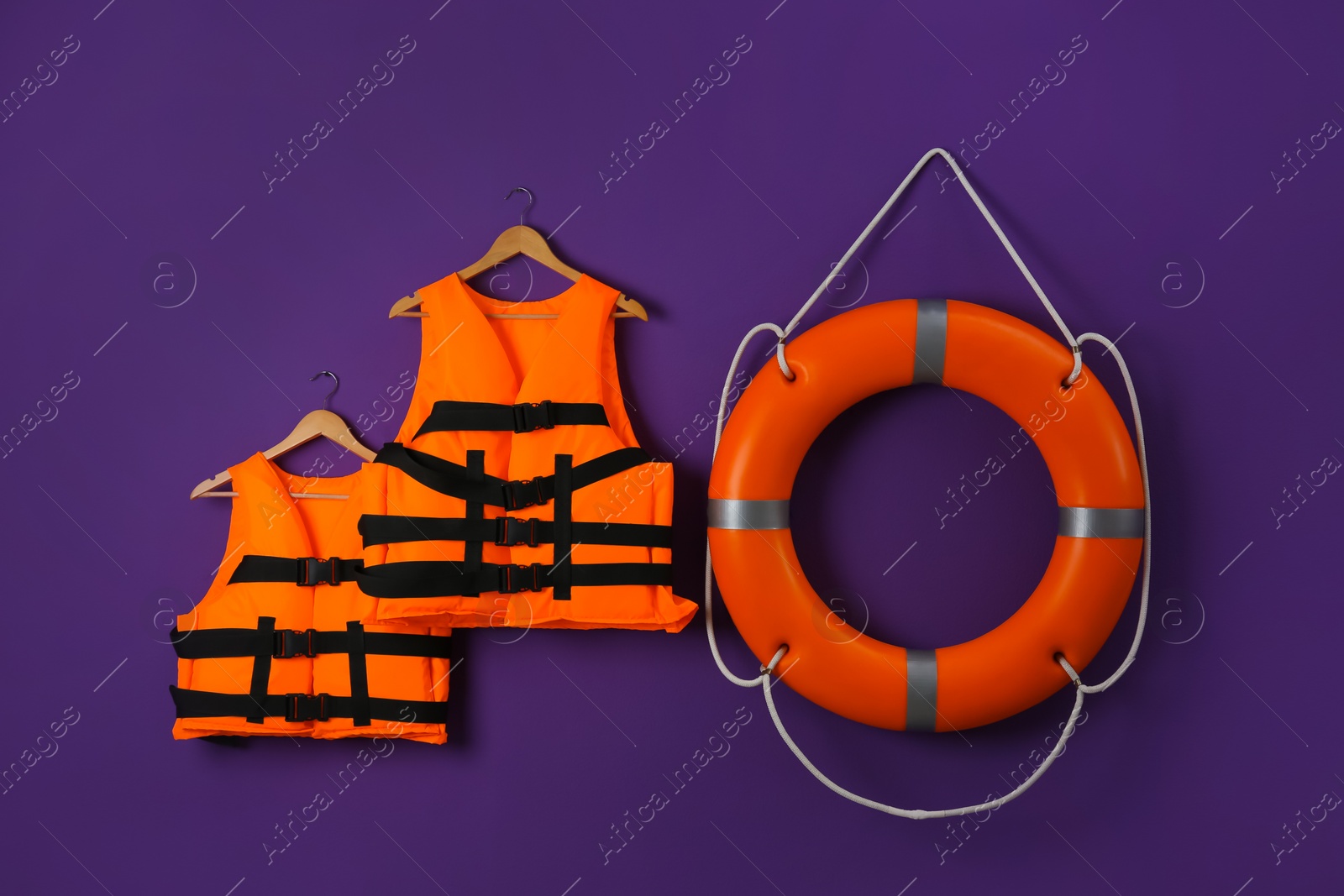 Photo of Orange life jackets and lifebuoy on violet background. Rescue equipment