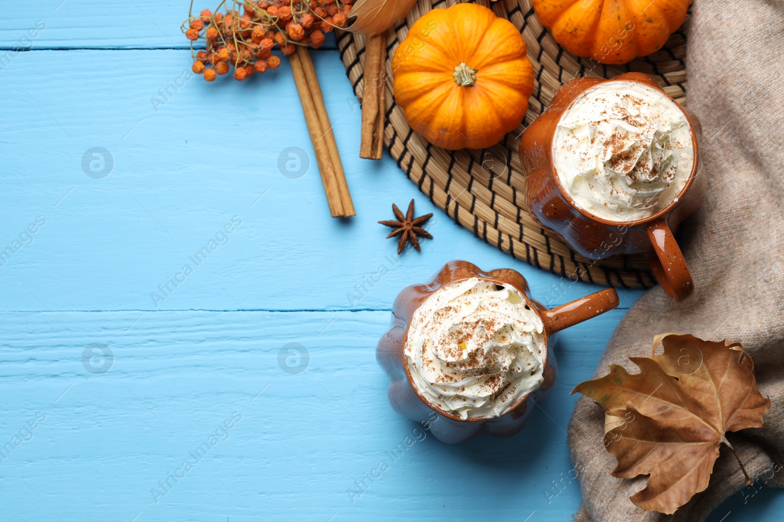 Photo of Flat lay composition with mugs of pumpkin spice latte on light blue wooden table. Space for text