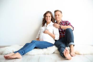 Photo of Pregnant woman with her husband near white wall. Space for text