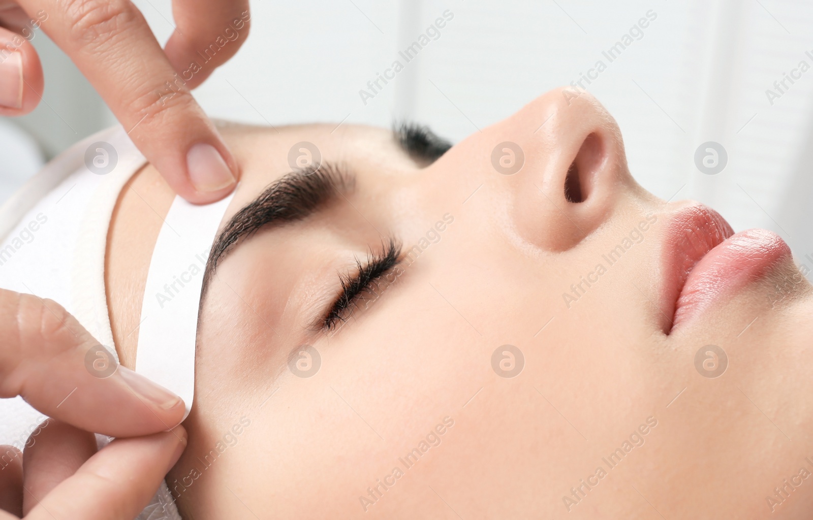 Photo of Young woman having professional eyebrow correction procedure in beauty salon, closeup