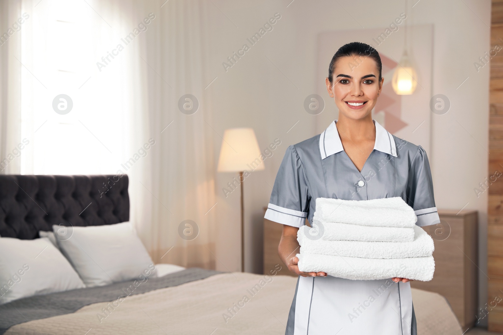 Photo of Chambermaid with stack of fresh towels in hotel room. Space for text