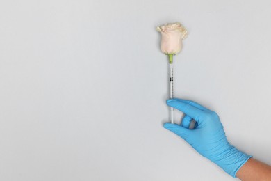 Photo of Doctor making injection to rose on light grey background, top view. Space for text