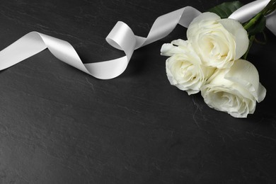 Photo of White roses and ribbon on black table, space for text. Funeral symbols