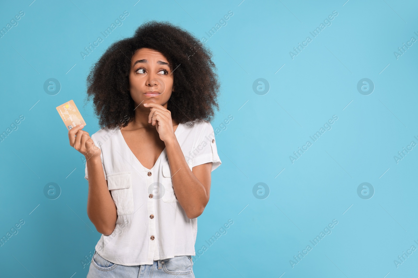 Photo of Confused woman with credit card on light blue background, space for text. Debt problem