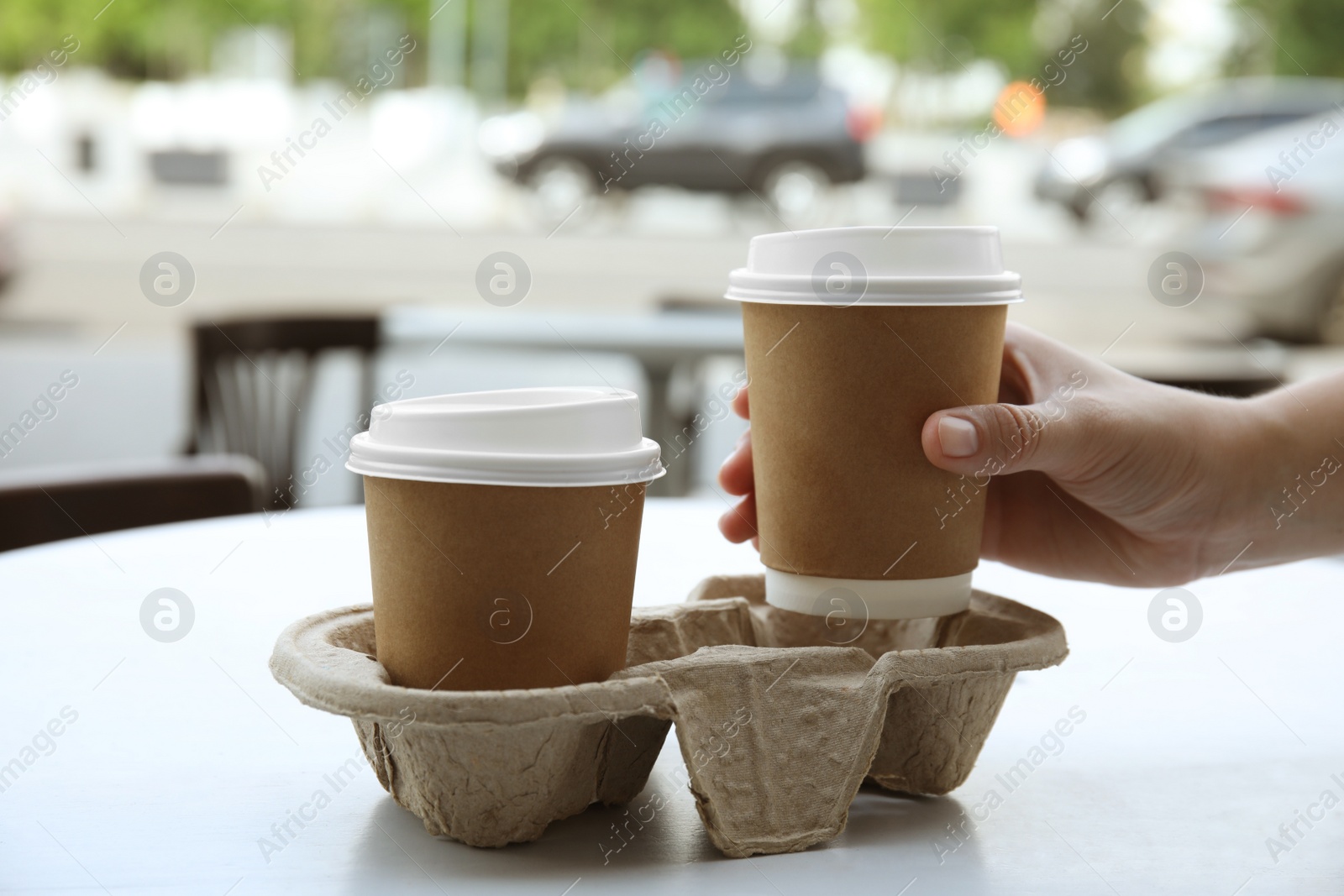 Photo of Woman taking paper coffee cup from cardboard holder at table outdoors, closeup