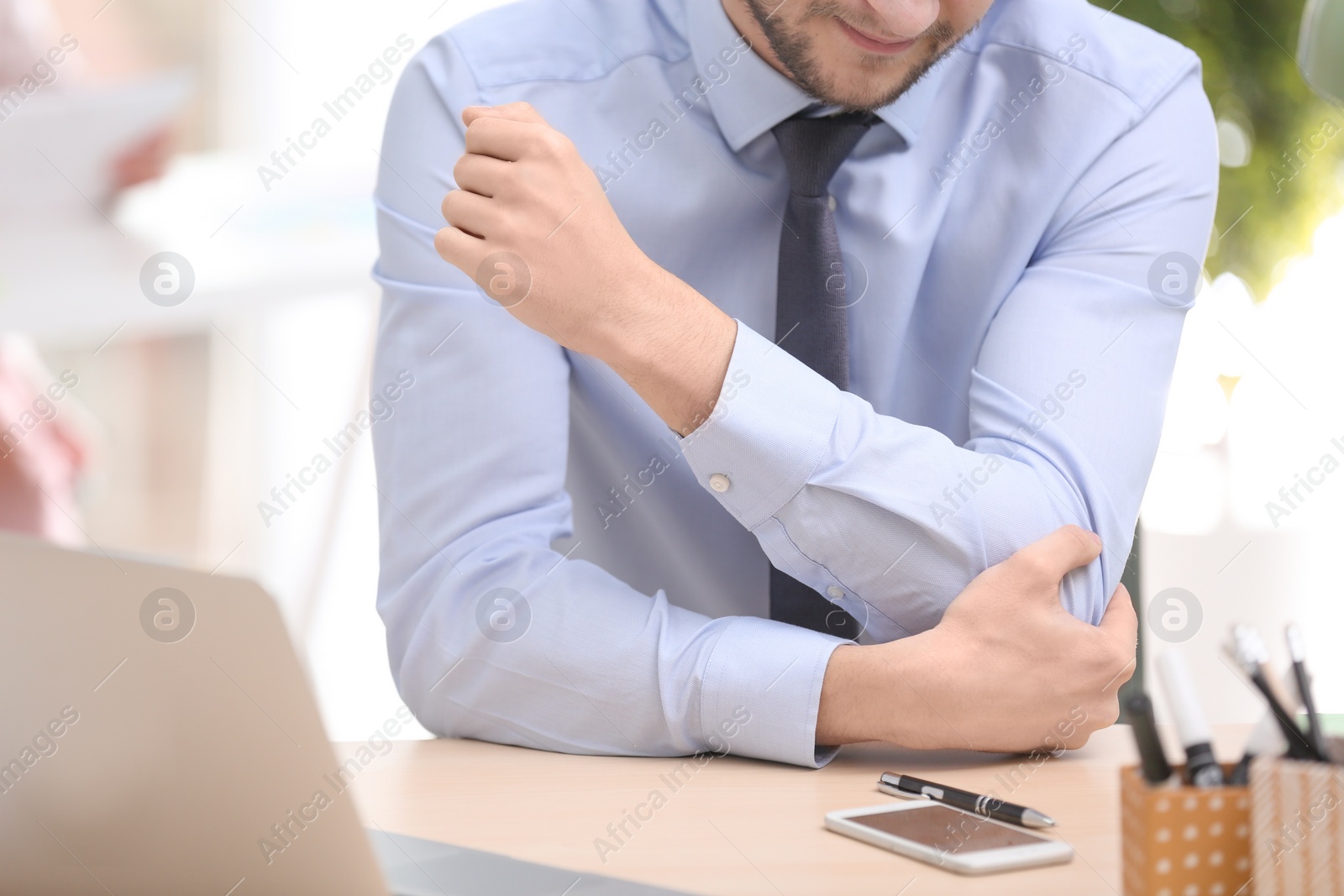 Photo of Young man suffering from elbow pain in office