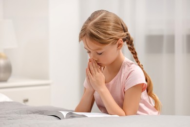 Girl holding hands clasped while praying over Bible in room