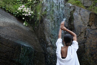 Photo of Young woman near beautiful waterfall outdoors, back view. Space for text