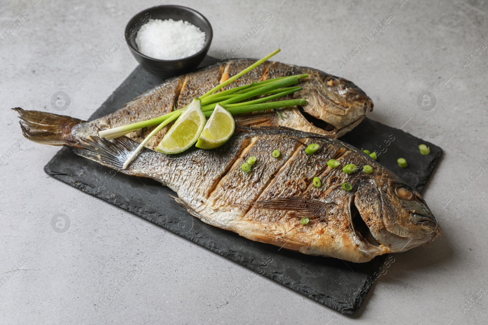 Photo of Seafood. Delicious baked fish served with green onion and lime on light textured table, closeup