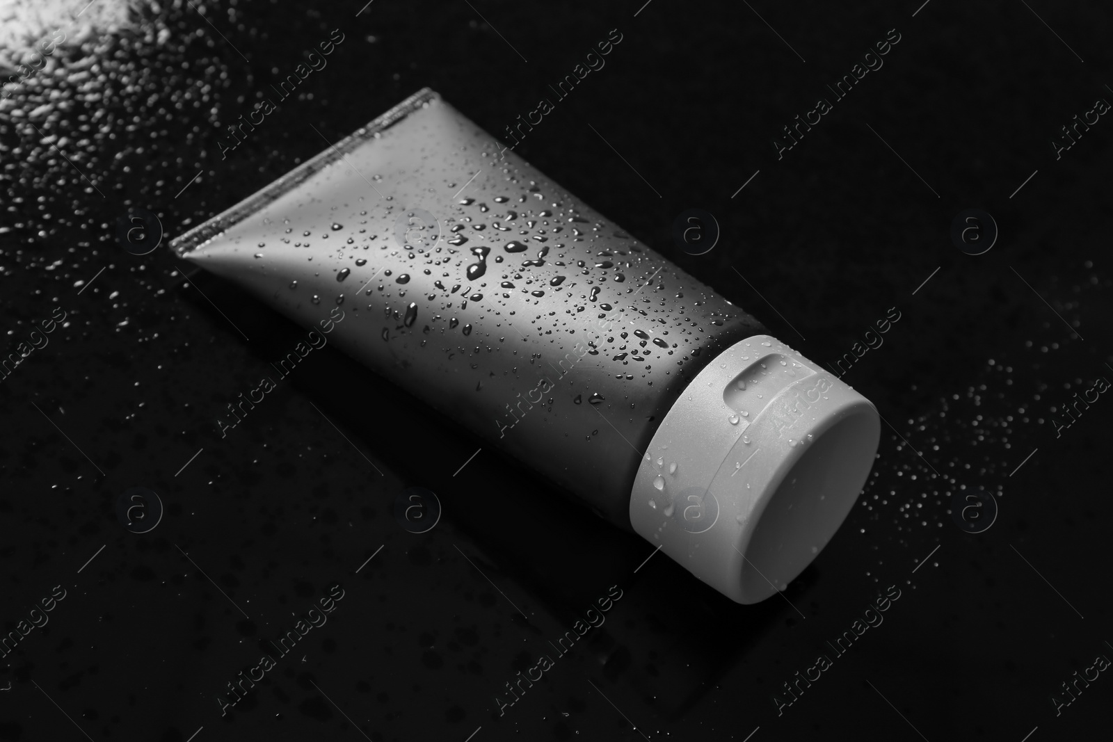 Photo of Tube on wet black surface, space for design. Men's cosmetic product