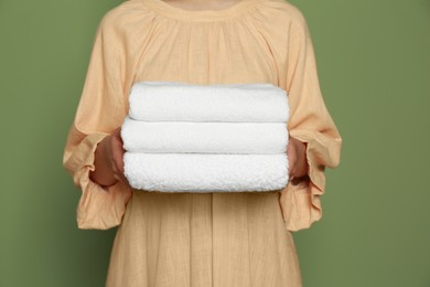 Photo of Woman holding folded soft terry towels on green background, closeup