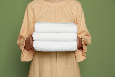 Woman holding folded soft terry towels on green background, closeup