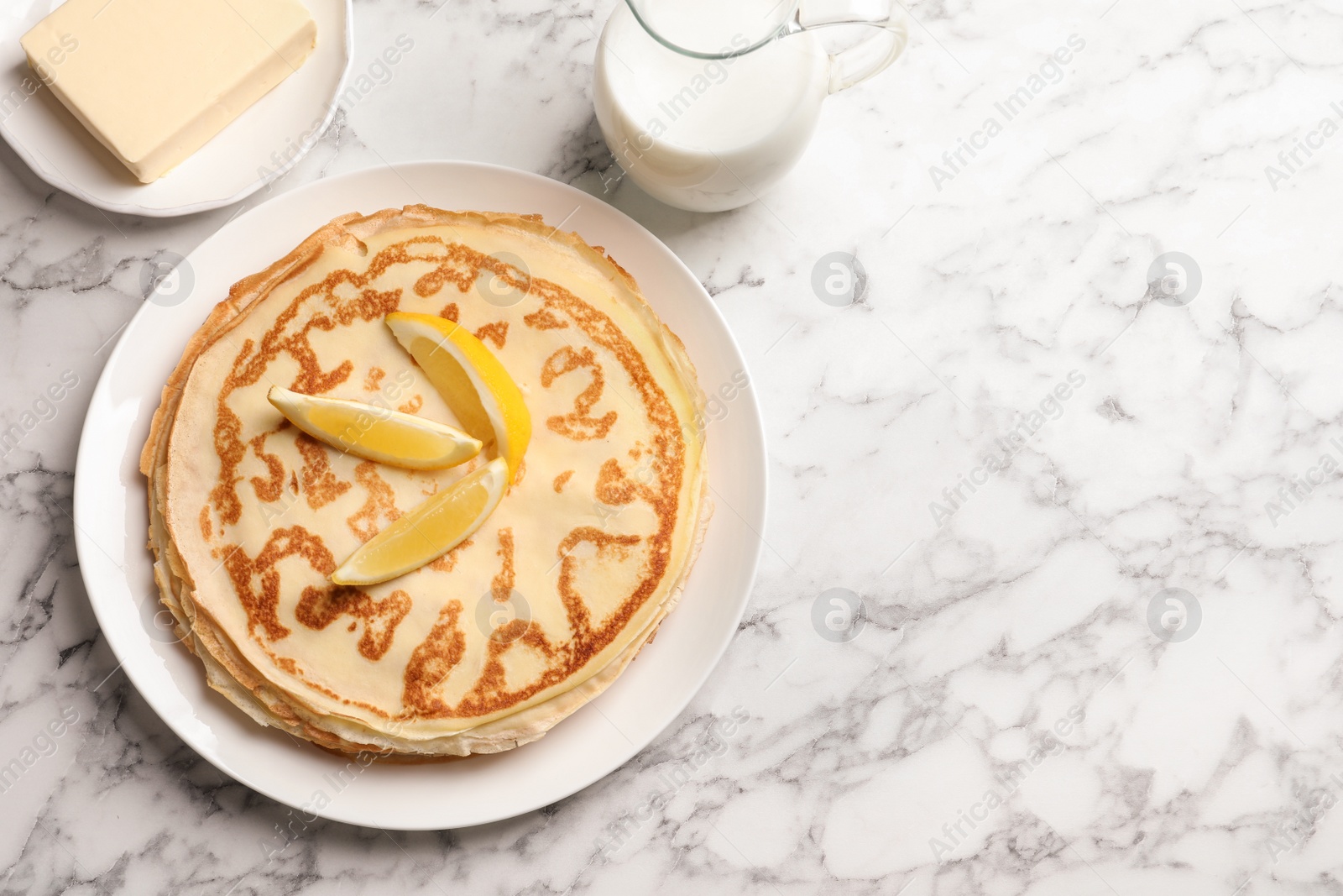 Photo of Thin pancakes with lemon, butter and milk on table, top view