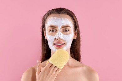 Happy young woman with face mask and sponge on pink background