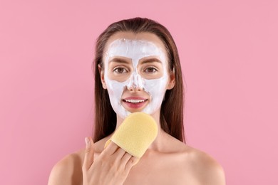 Photo of Happy young woman with face mask and sponge on pink background