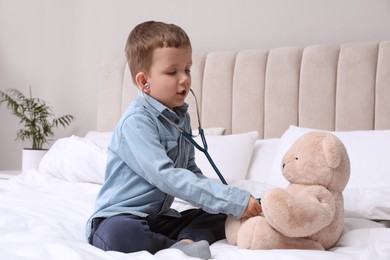 Photo of Cute little boy playing with stethoscope and toy bear in bedroom. Future pediatrician
